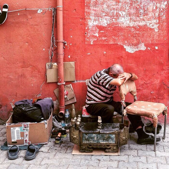 Man resting on a worn chair against a red wall, capturing candid life moments in Turkey by Yusuf Aksoy.