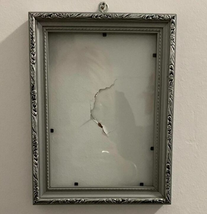 Empty ornate picture frame hanging on wall with a hole in the glass, showcasing one of the funniest parents ever moments.