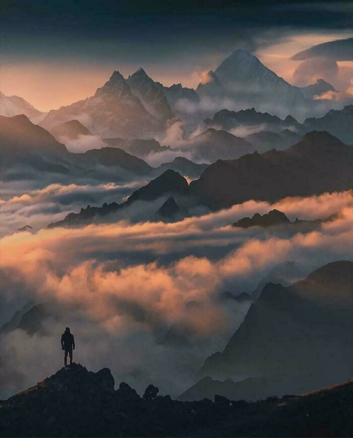 Amazing Photos - lone hiker on ridge overlooking layered misty mountains bathed in golden sunrise clouds