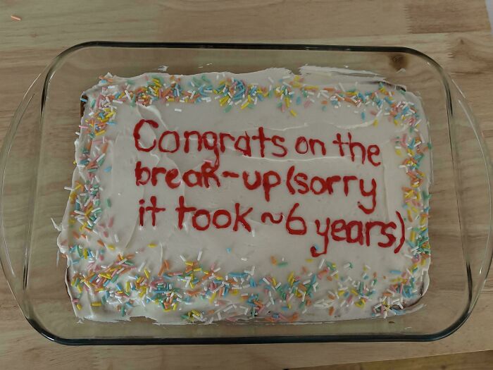 Rectangular homemade baked goods with white frosting, colorful sprinkles, and red icing text in a glass dish on a wooden surface.
