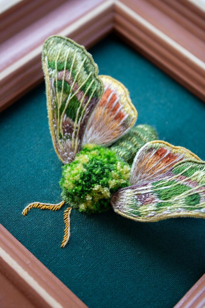 Detailed butterfly embroidery creation with textured wings in green, orange, and brown, framed for display.