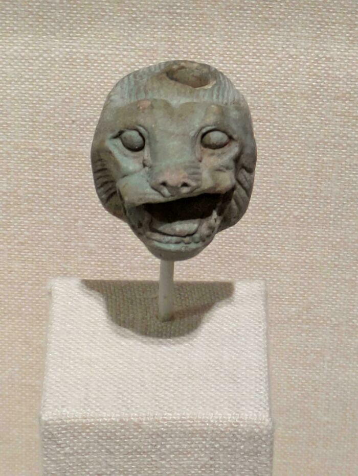 Ancient cat sculpture with mouth open as if meowing, displayed on a white stand against a neutral background.