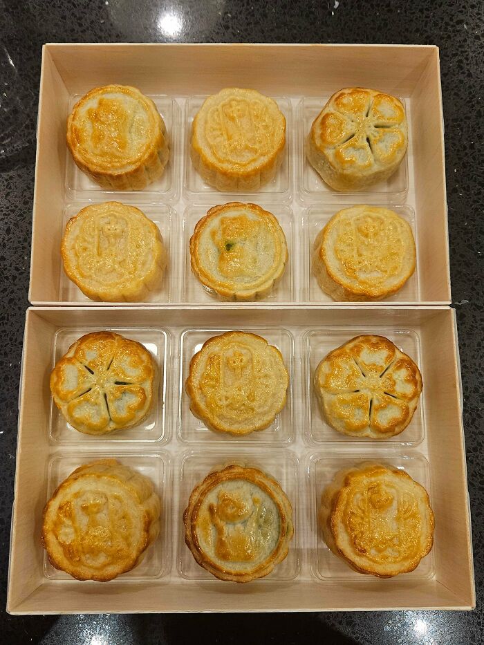 Box of golden baked goods arranged neatly in clear trays, showcasing beautiful detailed patterns and textures on each pastry.