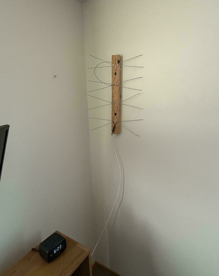 Homemade indoor antenna made from a wooden plank and metal wires mounted on a wall for signal reception.