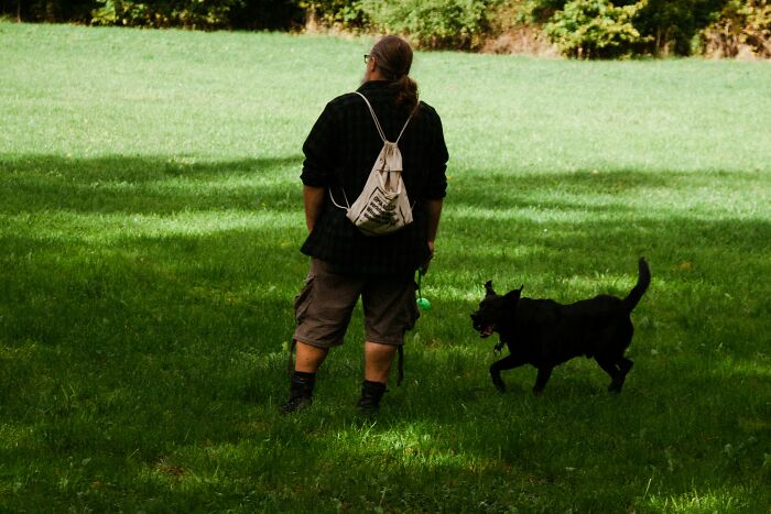 Person standing with a black dog on a leash in a grassy park, illustrating protection from a neighbor&rsquo;s dog incident.
