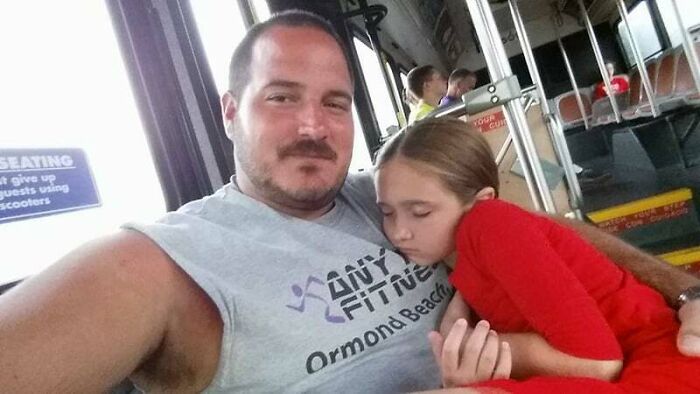 Man wearing a sleeveless shirt comforting a sleeping child on public transport, capturing heartwarming stories and kindness moments.
