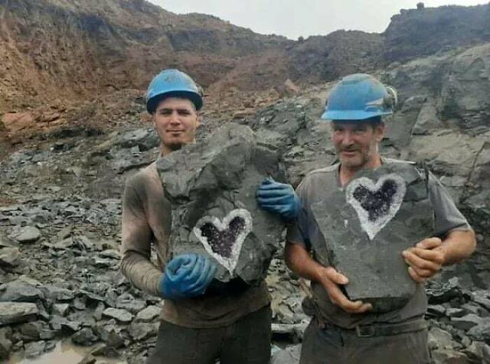 Two miners holding heart-shaped rocks, sharing a heartwarming moment in a rugged mining site.