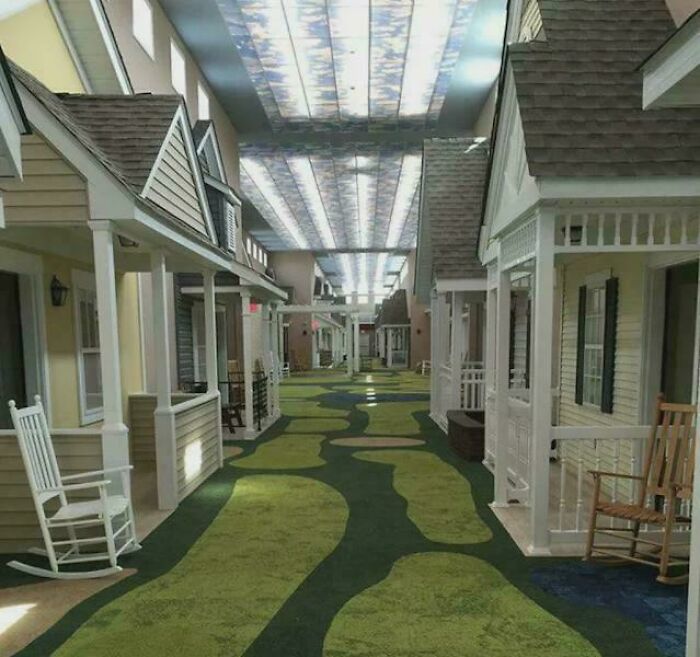 Indoor hallway designed like a neighborhood street with house facades and rocking chairs, evoking heartwarming stories.