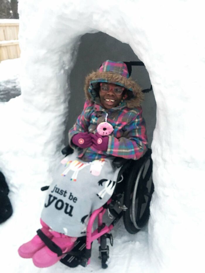 Child in a wheelchair smiling inside a snow fort, wearing colorful winter clothes in a heartwarming story setting.