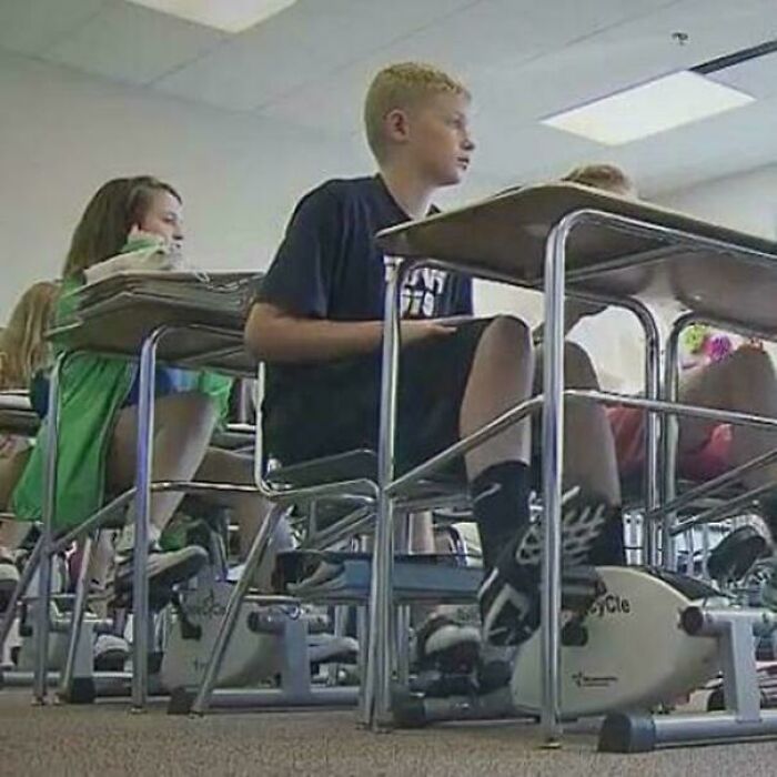 Students in a classroom using under-desk exercise bikes in a heartwarming story about positivity and uplifting moments.