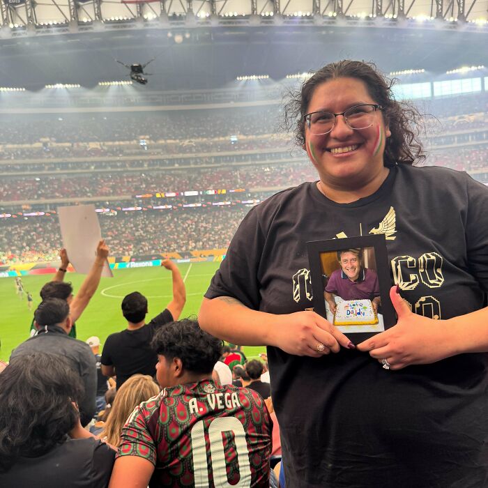 Smiling woman holding a framed photo at a crowded soccer stadium, showcasing heartwarming stories and positivity.