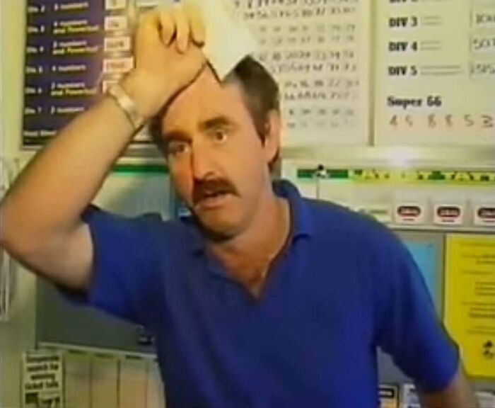 Man in blue shirt wiping sweat from forehead, expressing relief while standing in front of a bulletin board of heartwarming stories.