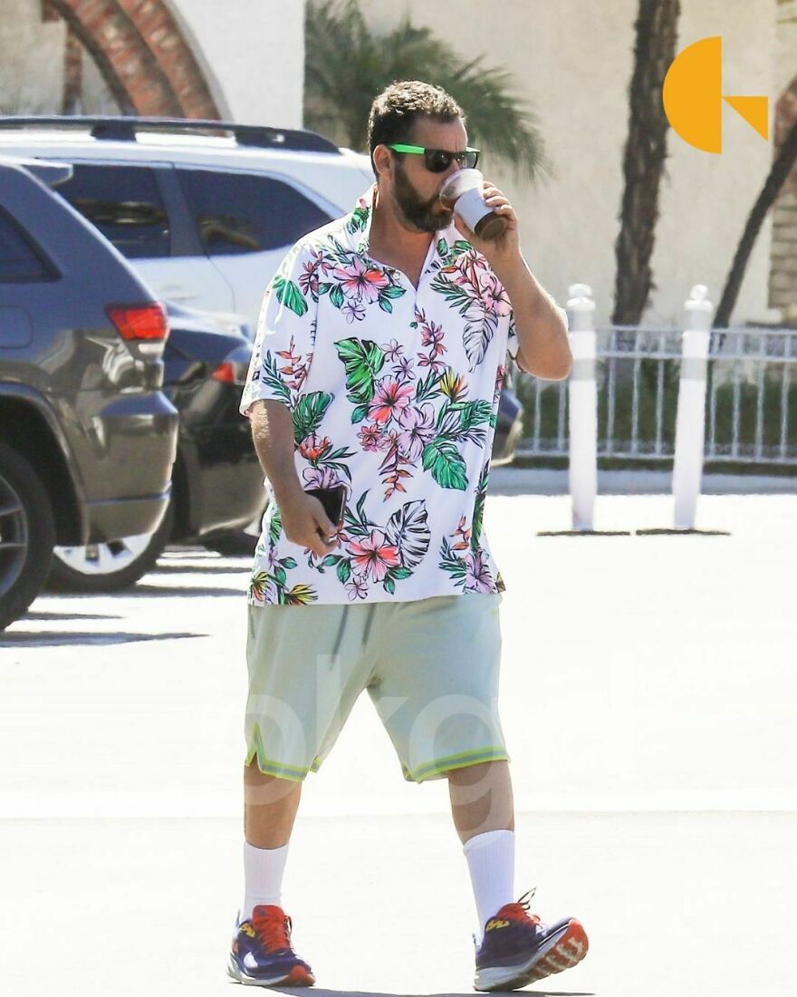 Adam Sandler wearing floral shirt and shorts outdoors, drinking coffee, showcasing a casual outfit for readers’ vote on outfits.
