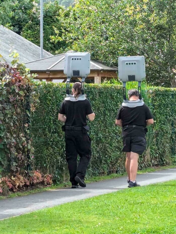 Two people walking outdoors wearing head-mounted devices in a dystopian real-life US scene.