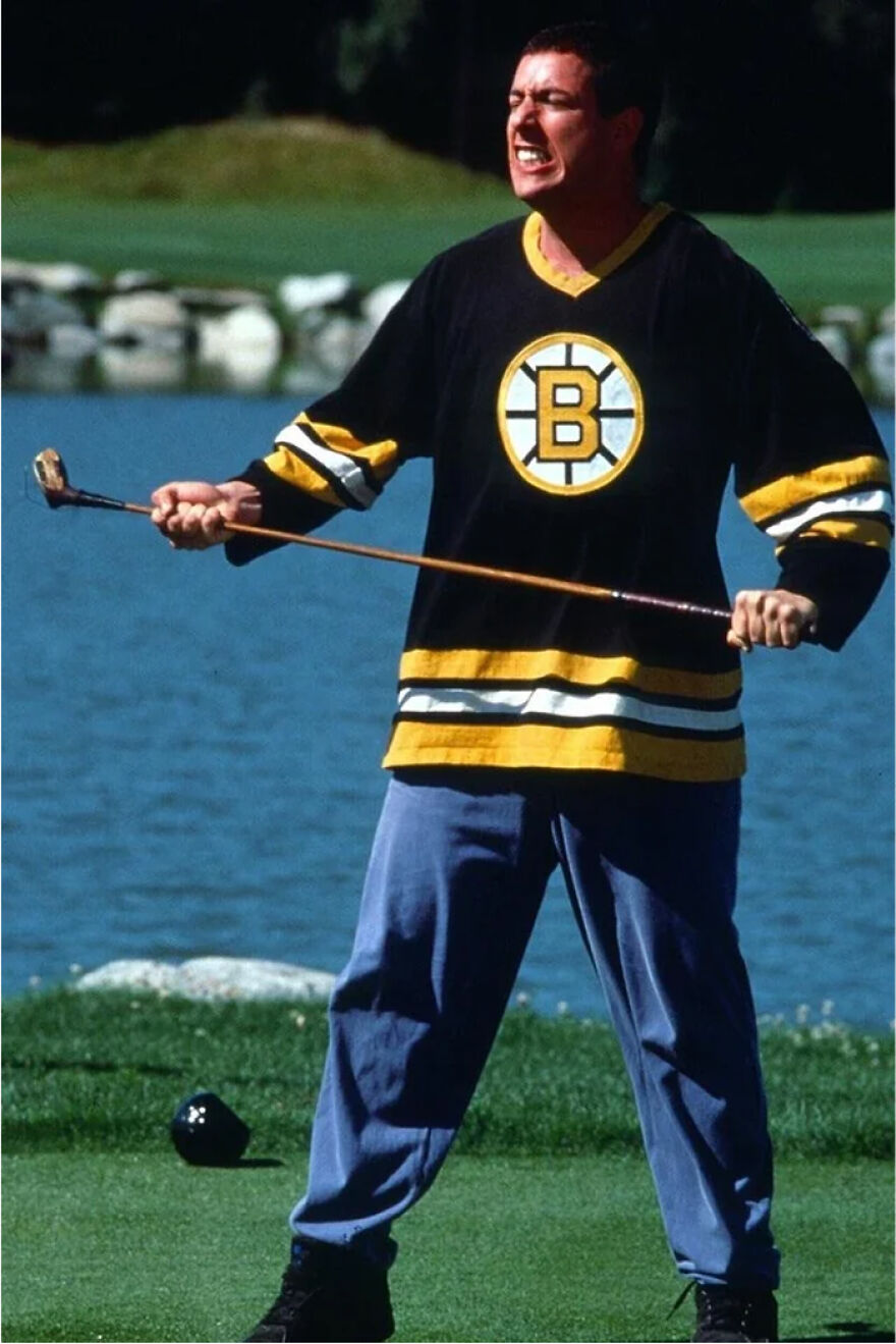 Adam Sandler wearing a Boston Bruins hockey jersey on a golf course, gripping a golf club with an intense expression.