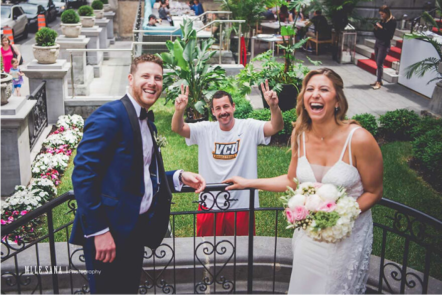 Happy bride in white dress and groom in navy suit posing outdoors with man in casual outfit making peace signs behind them