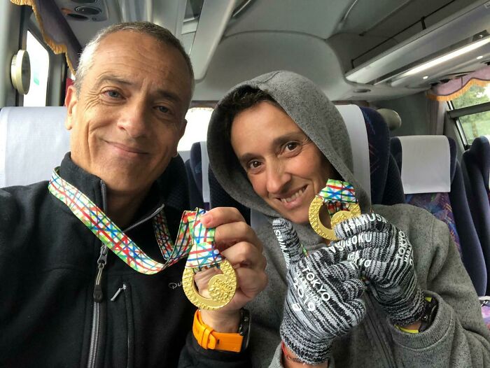 Two parents proudly showing their colorful gold medals on a bus, capturing funny and wholesome moments.