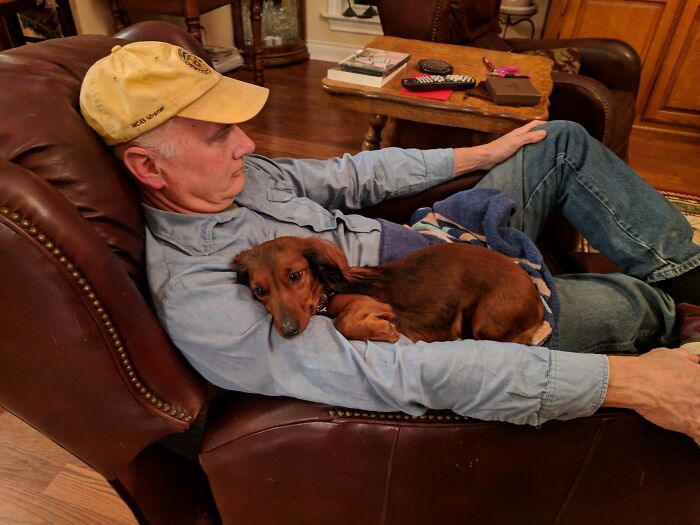 Older man relaxing on a recliner with a dog on his arm, showcasing funny and wholesome parent moments shared by kids.