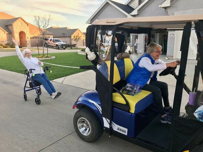 Elderly parent in a golf cart playfully pulling another parent with a walker, showcasing funny and wholesome moments shared by kids.