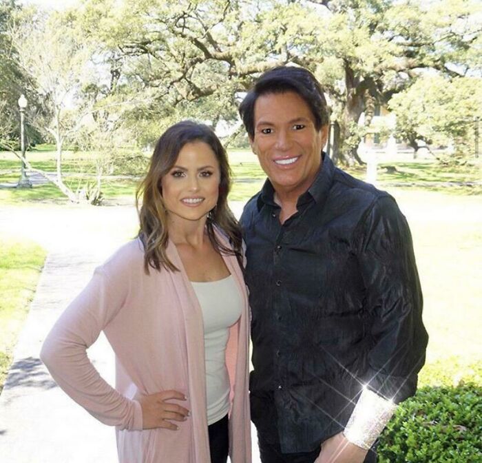 Two influencers posing outdoors in casual clothing with trees and a pathway in the background.