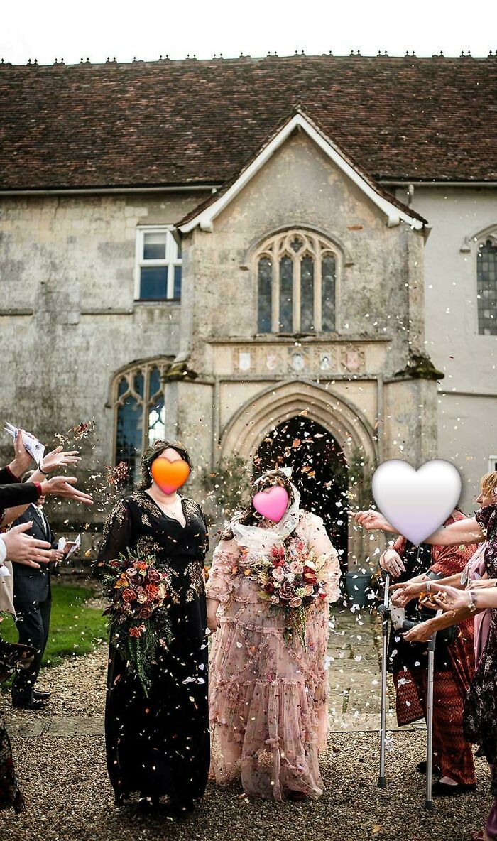 Wedding brides and guests walking outside historic church while being showered with confetti by guests.