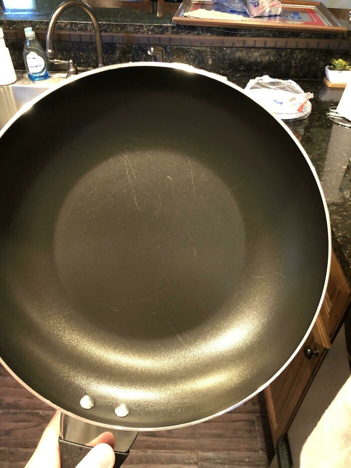 Scratched nonstick pan held over kitchen sink, illustrating awful roommates neglecting cookware care.
