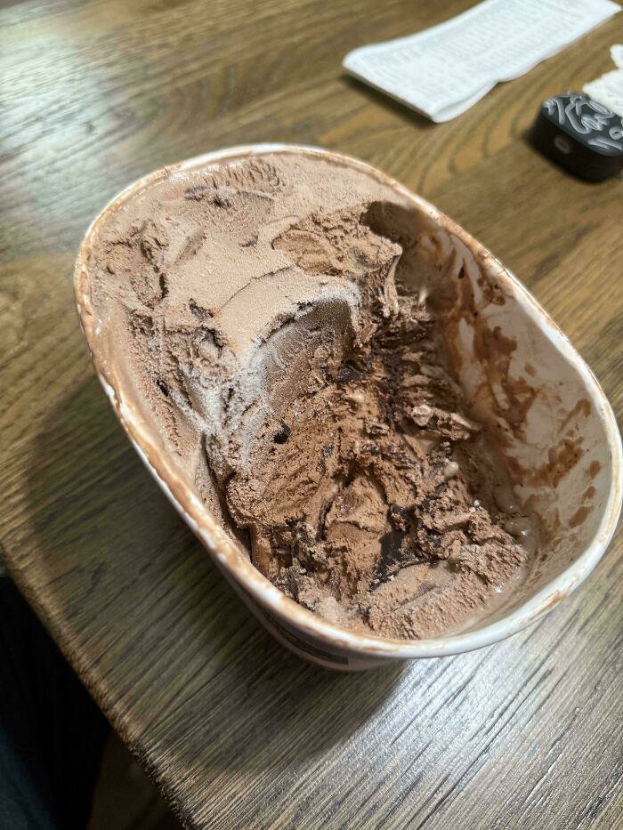 Partially eaten chocolate ice cream container left on a wooden table showing signs of awful roommates behavior.