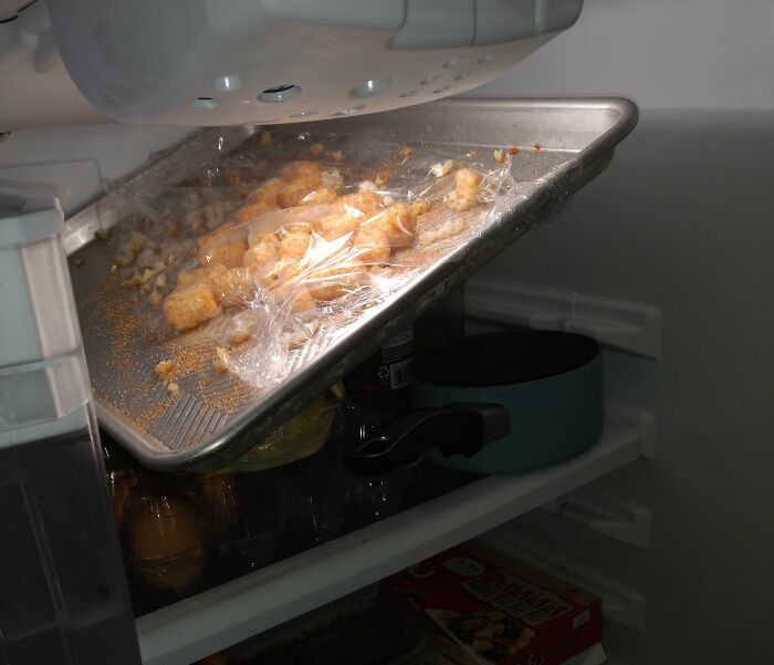 Baking sheet left inside fridge with leftover food wrapped in plastic, illustrating awful roommates’ bad habits.