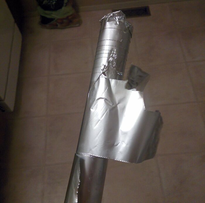 Damaged aluminum foil roll held upright, showing torn and unraveled edges in a kitchen setting, illustrating awful roommates.