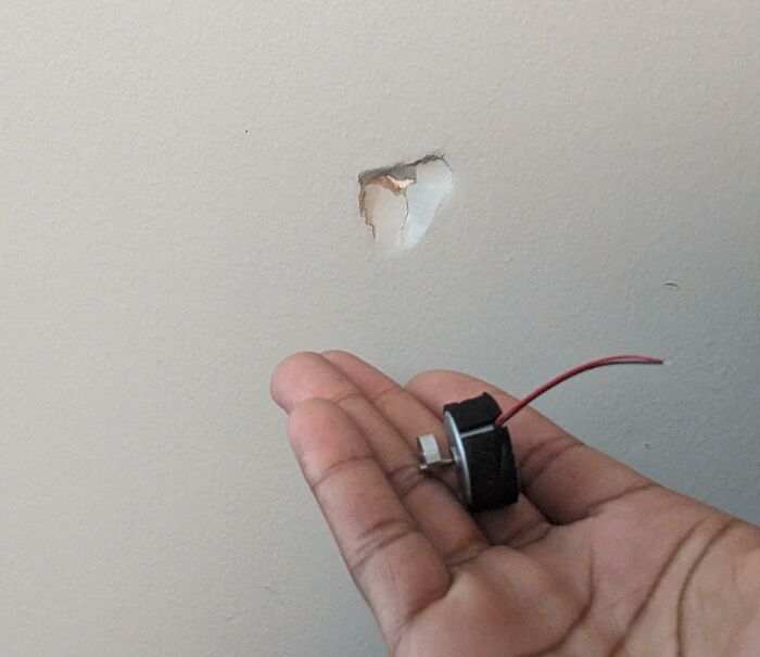 Hand holding a broken fan part in front of a wall with a hole, illustrating awful roommates damaging property.