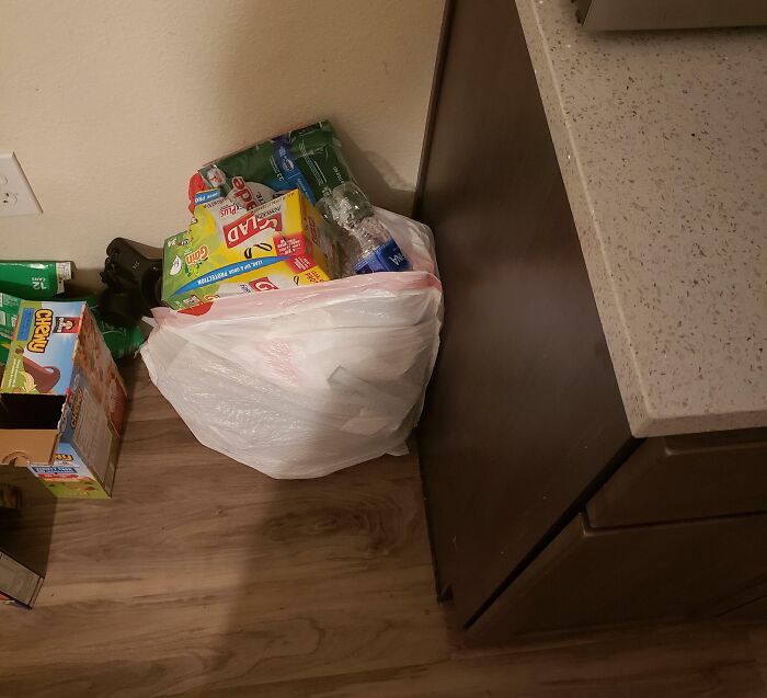 Overflowing trash bag and scattered food boxes on floor in kitchen, illustrating awful roommate mess and lack of cleanliness.