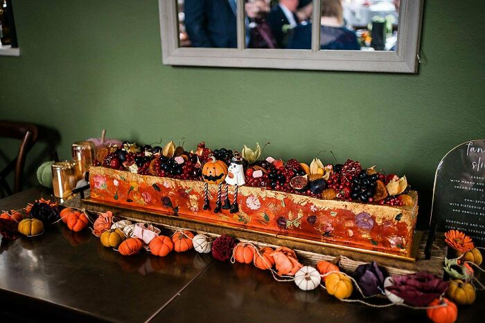 Long rectangular baked goods decorated with fresh berries, fruit, and Halloween-themed cake toppers on a table display.