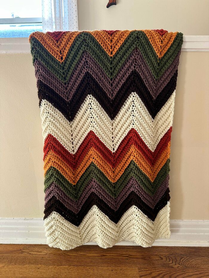 Chevron patterned crochet blanket draped over a white ledge, showcasing mastery in crocheting colorful yarn.