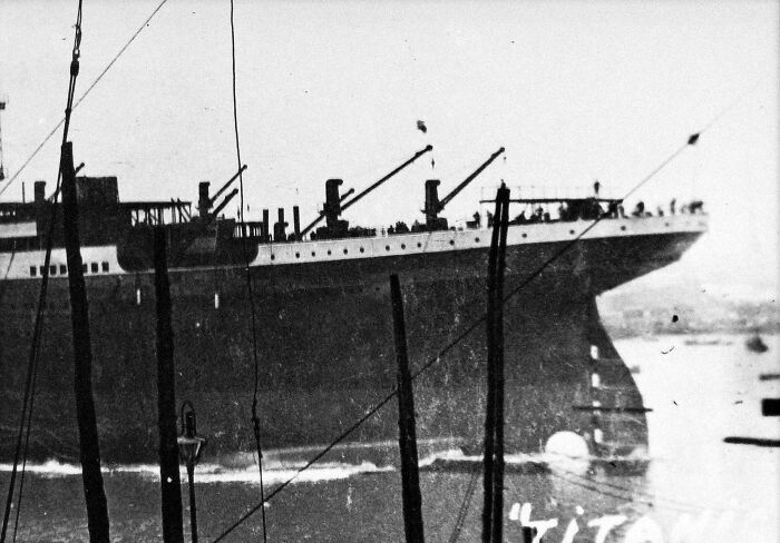 Rare historical photo of the Titanic captured from a harbor, showing the ship’s bow and deck details in black and white.