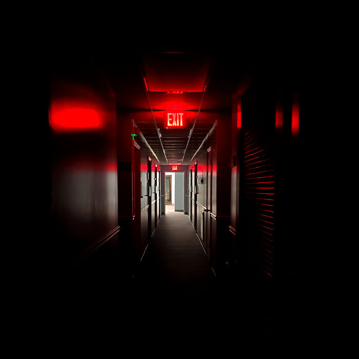 Dimly lit hallway with red exit signs creating a creepy scene, illustrating unsettling photos from jobs that should pay more.