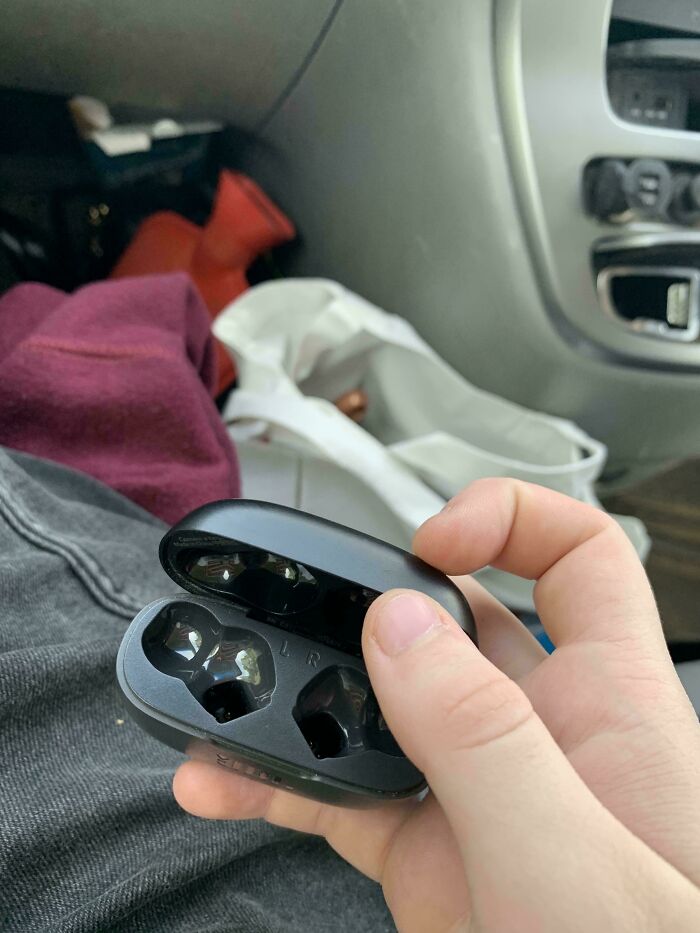 Black wireless earbuds case held in hand with both earbuds missing, illustrating worst luck on vacation moment.