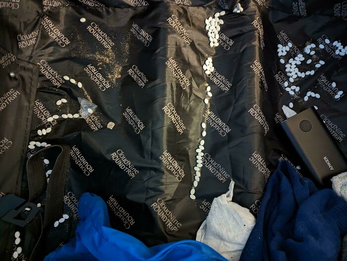 White pills spilled across black luggage lining, showing worst luck on vacation mishap with scattered belongings.