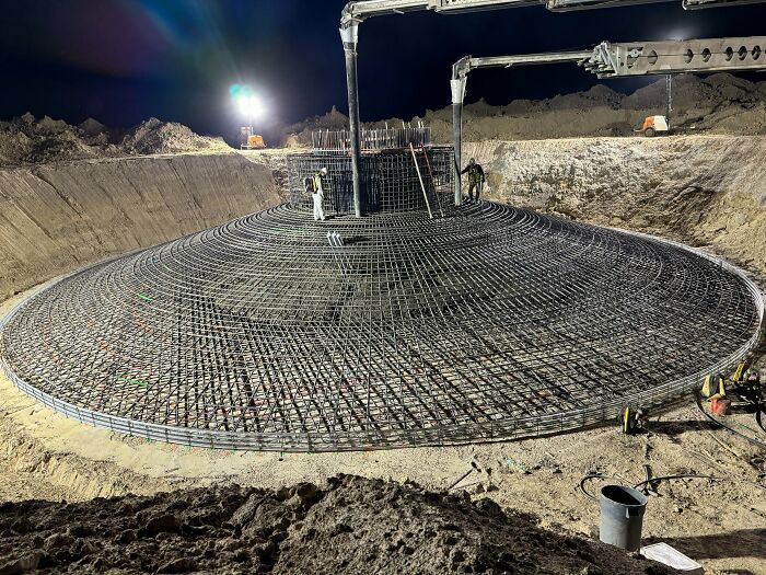 Workers pouring concrete over large steel rebar structure at night on a construction site, highlighting jobs that should pay more.