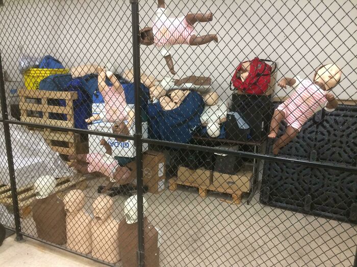 Storage room with creepy baby dolls suspended behind a mesh fence, highlighting unsettling jobs that should pay more.