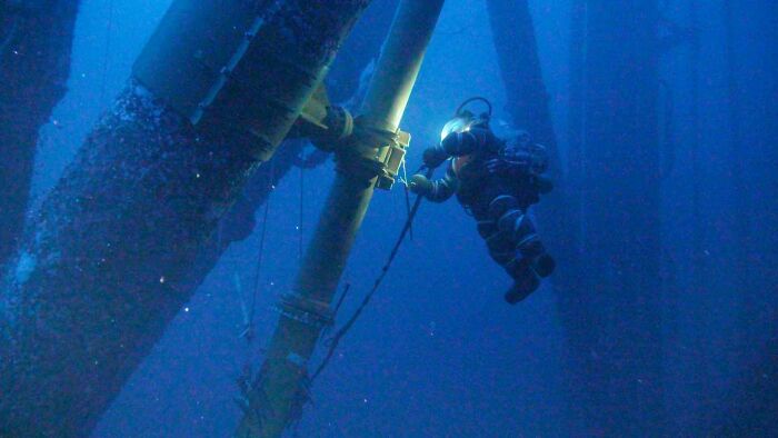 Underwater commercial diver working on oil rig supports in deep blue water, illustrating jobs that should pay more.