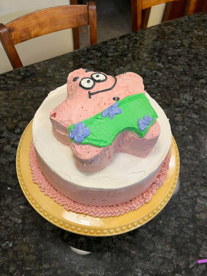 Pink character-shaped cake with green and purple icing decorations on top of a round white frosted baked good.