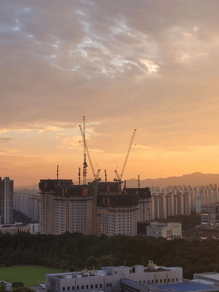 Urban hell scene with high-rise buildings under construction and cranes at sunset in a dense cityscape.