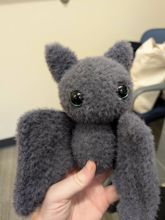 Hand holding a crocheted fluffy gray bat with large eyes, showcasing a creative crocheting project.