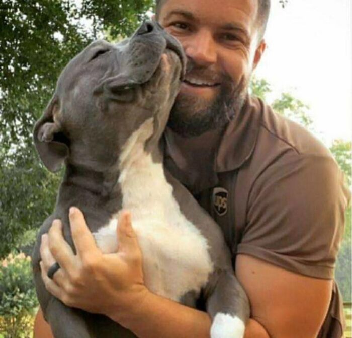 UPS driver smiling and hugging an adorable gray and white dog outdoors, showcasing a heartwarming pet encounter.