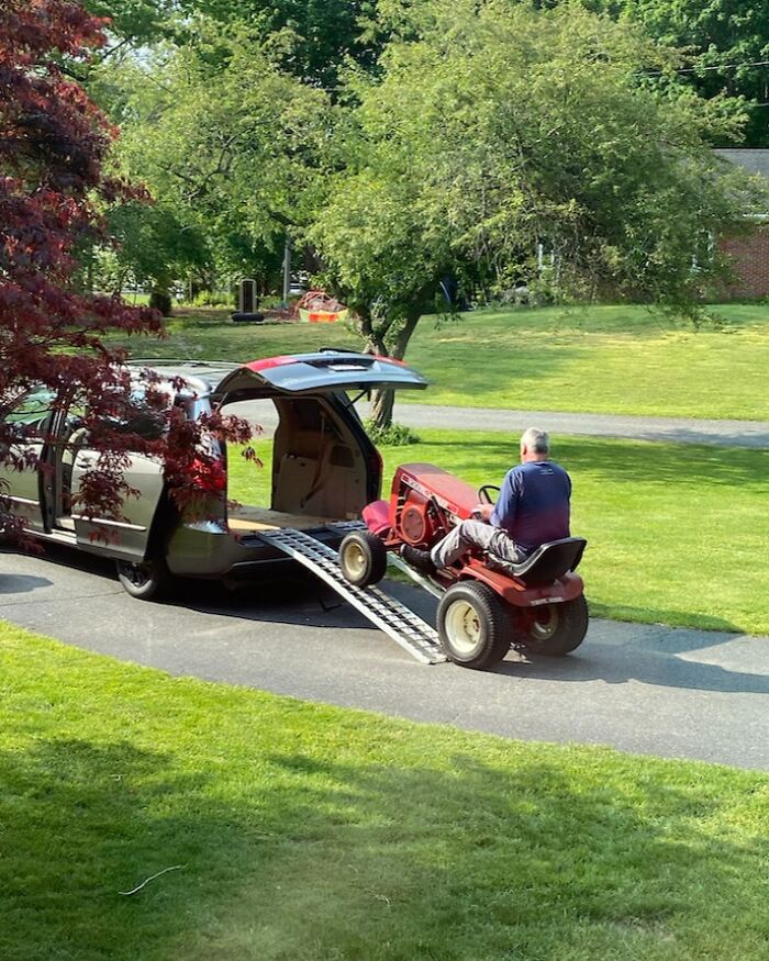 Man driving a lawn tractor up a ramp into a van, showcasing one of the funniest parents ever in a humorous moment outdoors.
