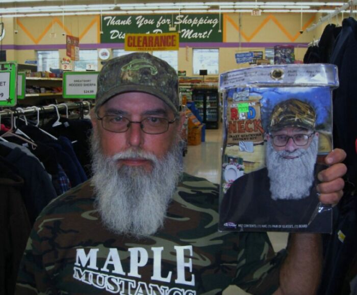 Man with long white beard and camouflage hat holding a humorous redneck costume beard in a store, funny parents humor.