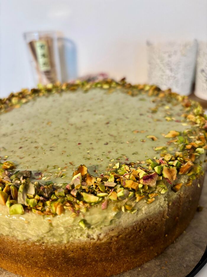 Close-up of a gorgeous baked good featuring creamy pistachio topping and crushed nuts on a golden crust.