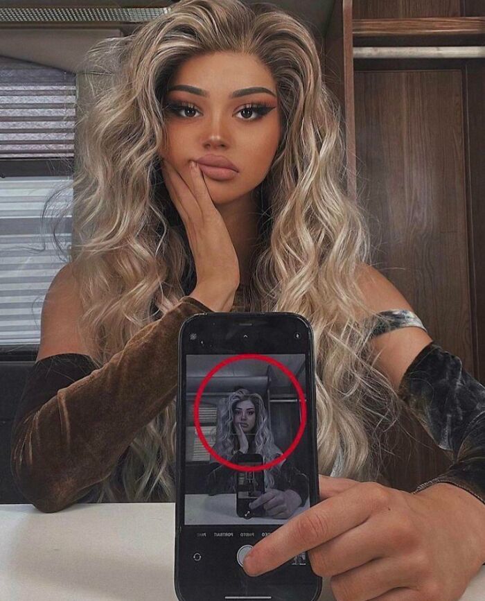 Influencer taking a selfie with phone displaying an edited image, showcasing unrealistic beauty standards and influencer culture.