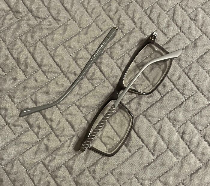 Broken eyeglasses with a detached arm on a gray quilted surface, illustrating worst luck on vacation moments.