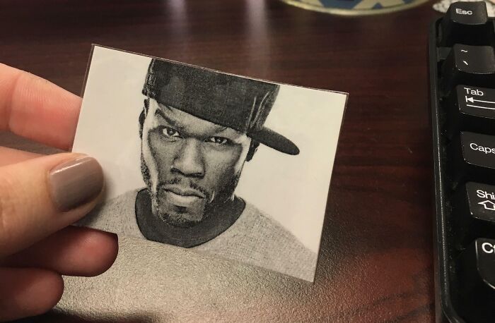 Hand holding a small black and white photo of a man in a cap, on a desk near a computer keyboard, funny teachers humor.